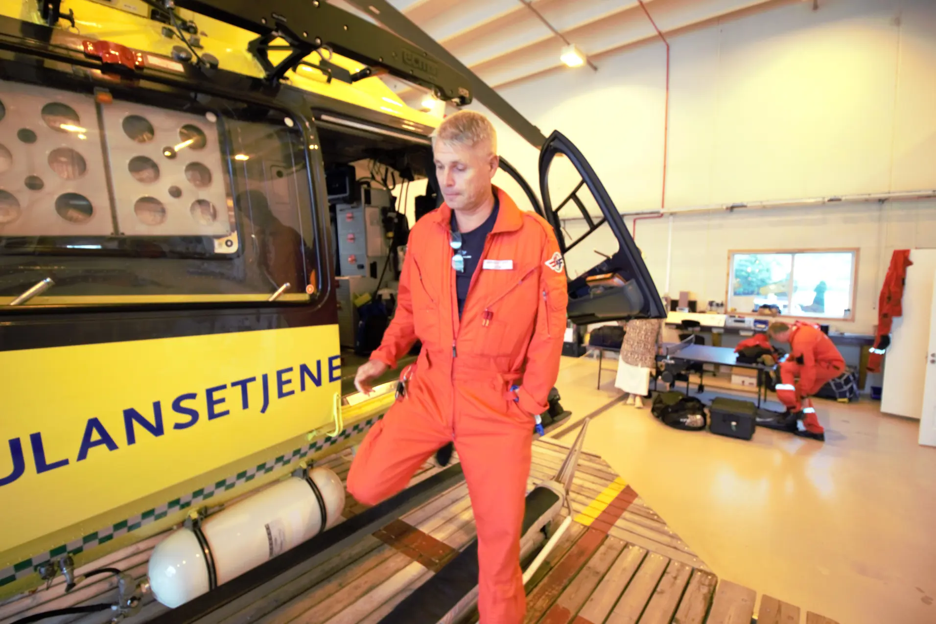 En mann i rød jumpsuit som står ved siden av et helikopter